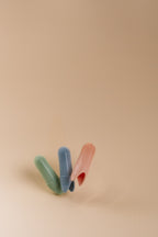 Three textured silicone finger brush accessories in green, blue, and orange, arranged in a fan shape on a solid beige background.