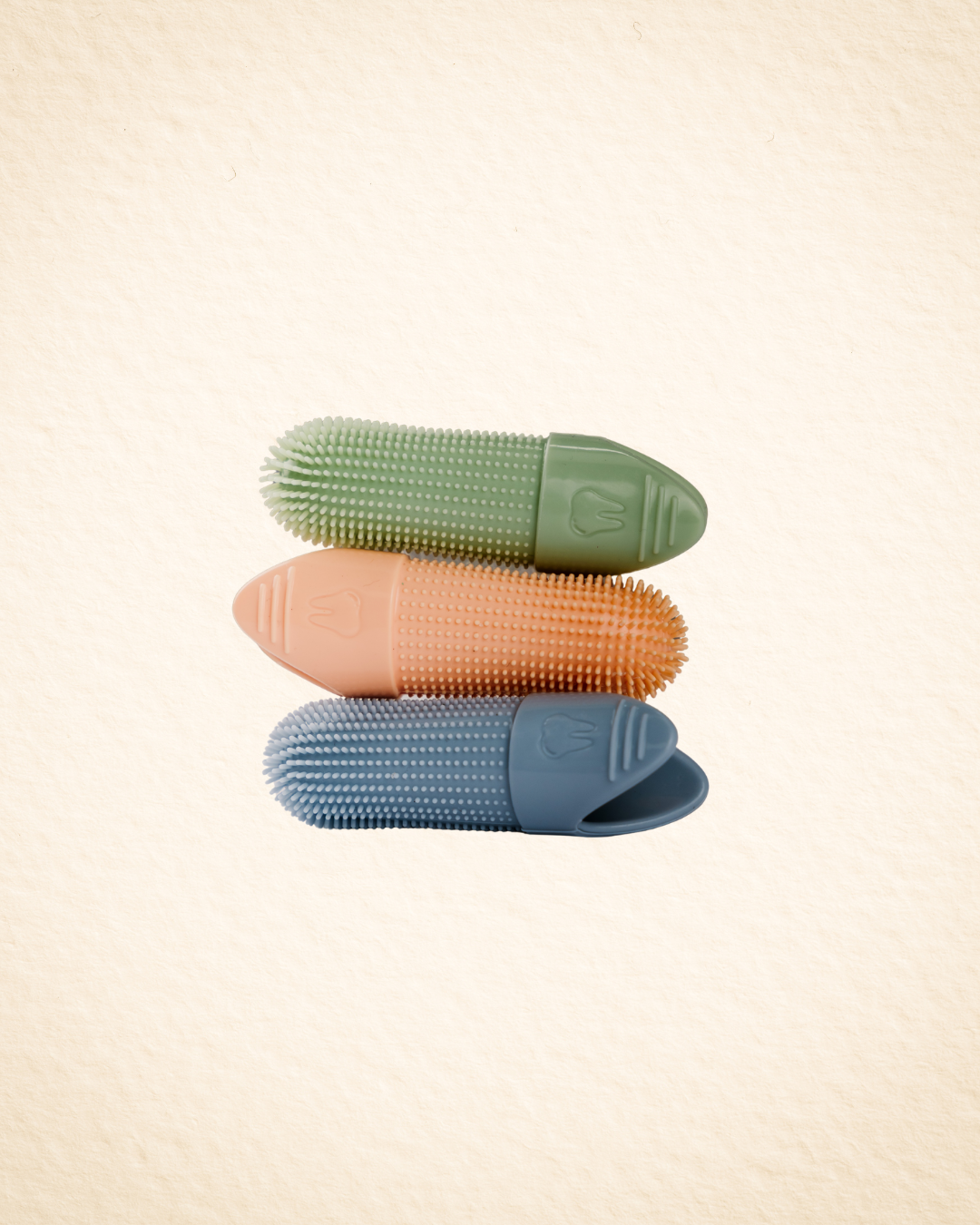 Three textured silicone slip-on finger brushes in crisp green, orange, and sky blue, stacked vertically on a light beige textured background.